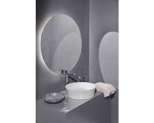 Salle de bains avec miroir rond, lavabo à poser, robinetterie et meuble sous-lavabo