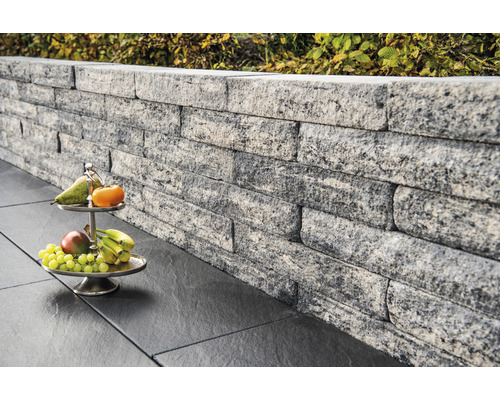 Mur en pierres grises avec un plateau de fruits sur des dalles de sol foncées