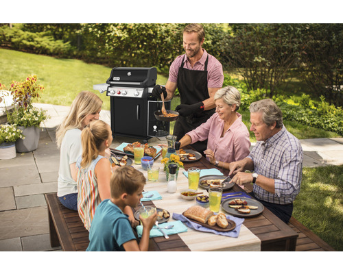 Eine Familie geniesst ein Grillfest mit einem Gasgrill im Garten.