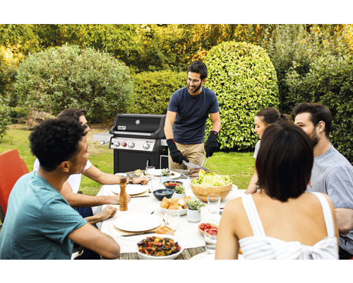 Szene mit einer Gruppe von Personen, die im Garten um einen Tisch sitzen und grillen.