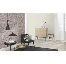 Wohnzimmer mit floral gemusterter Tapete, Sessel, Beistelltischen und Holzschrank