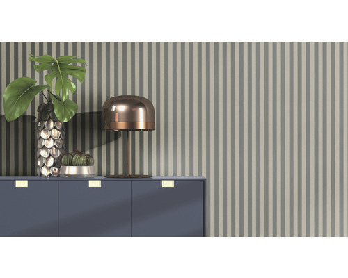 Arrangement décoratif avec lampe de table, vase, plante et cactus sur une armoire devant un papier peint rayé.