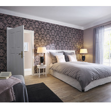 Schlafzimmer mit gemusterter Tapete, Bett, Nachttischen und Lampen.