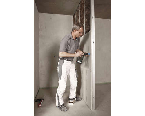 Ein Mann befestigt eine Trockenbauwand mit einem Schraubenzieher in einem Raum.