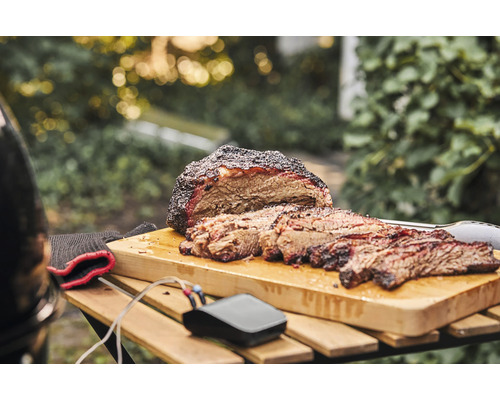 Brisket tranché sur une planche à découper avec thermomètre et ustensiles de barbecue