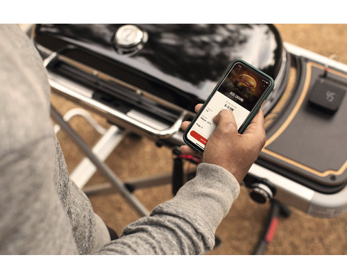 Une personne utilise une application sur un smartphone à côté d''un barbecue.