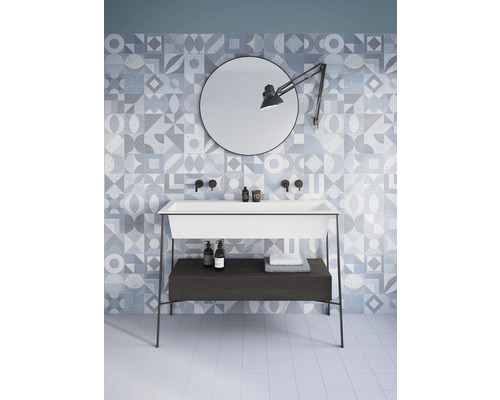 Badezimmer mit weißem Waschtisch, rundem Spiegel und geometrischen Fliesen an der Wand