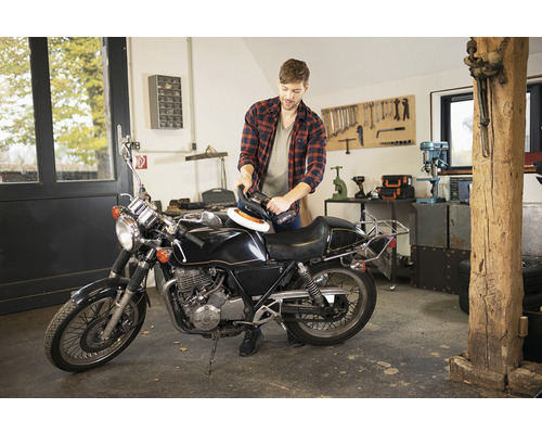 Homme polissant une moto avec une polisseuse dans un atelier
