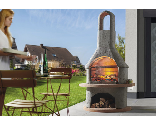 Espace barbecue maçonné avec bois de chauffage et salon de jardin sur pelouse