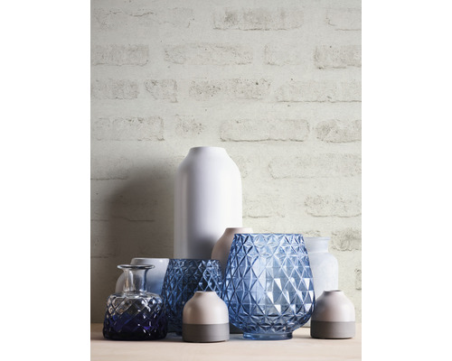 Dekorative Vasen aus Glas und Keramik auf einem Tisch vor einer Ziegelwand