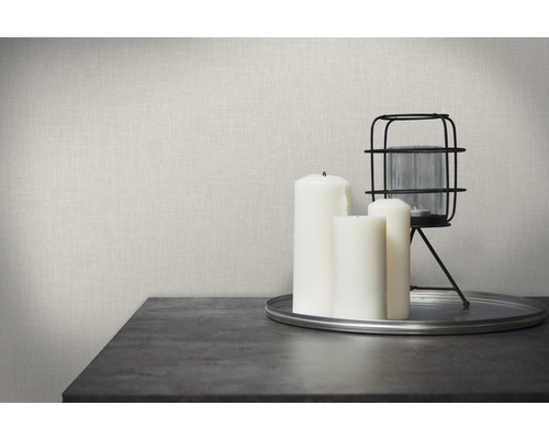 Scène décorative avec papier peint imitation lin, bougies et lanterne sur une table.