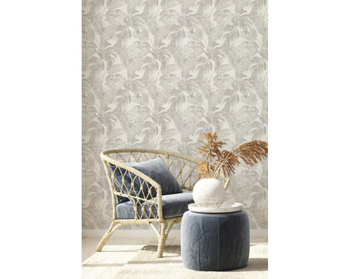 Pièce décorative avec papier peint à motifs, fauteuil en rotin et tabouret.