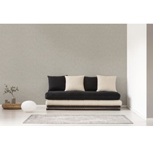 Helles Zimmer mit einer Couch, mehreren Kissen, einem kleinen Tisch, einer Lampe und einem Teppich.