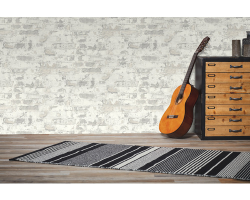 Chambre décorative avec guitare, tapis et commode devant un papier peint à l''aspect maçonnerie.