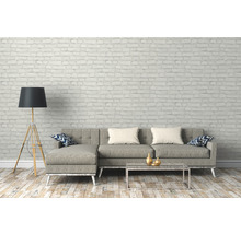 Salon avec canapé gris, lampadaire et table basse devant un mur de briques