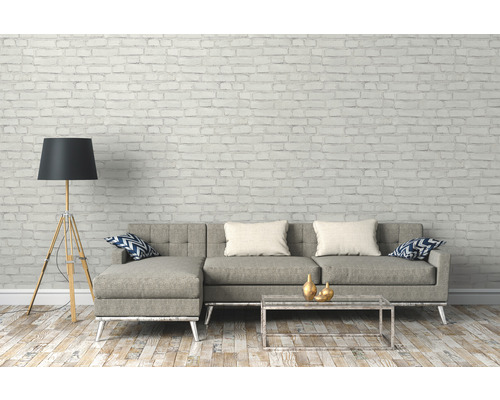 Salon avec canapé gris, lampadaire et table basse devant un mur de briques