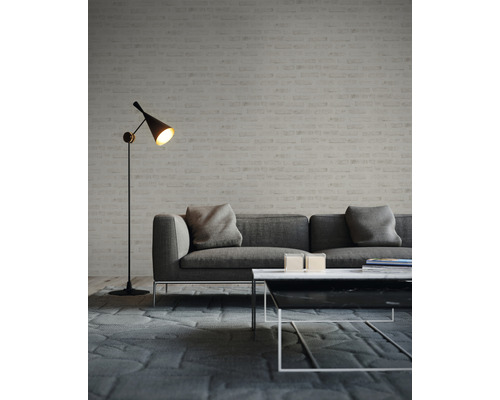 Wohnzimmer mit grauem Sofa, Couchtisch und Stehlampe vor einer Ziegelwand