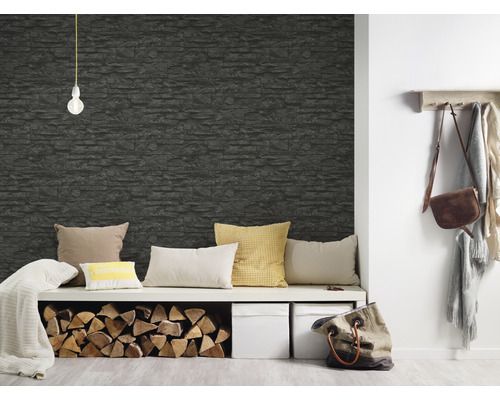 Wohnraum mit einer Wandtapete in Steinoptik, einem Sitzmöbel, Kissen und Brennholz.