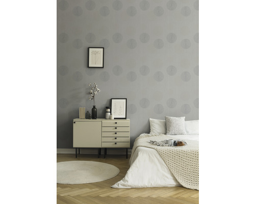 Chambre avec papier peint gris, commode et lit.