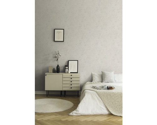 Heller Raum mit beiger Kommode und Bett vor einer gemusterten Wand