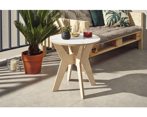 Scène avec une table d''appoint ronde en bois, un canapé en palettes avec coussins et une plante d''intérieur en pot sur un balcon.