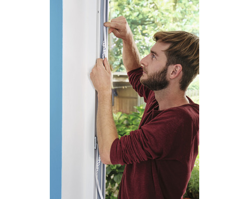 Ein Mann befestigt ein Dichtungsband an einem Fensterrahmen.