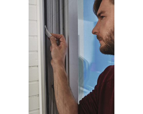 Ein Mann bedient ein Insektenschutzrollo für Fenster.