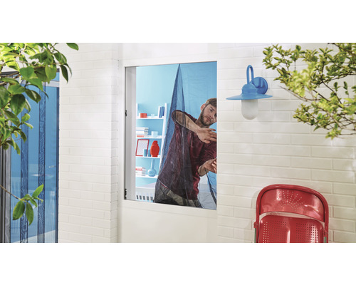 Ein Mann installiert ein Insektenschutzgitter an einem Fenster in einem hellen Raum.