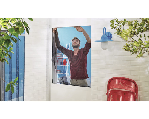 Mann befestigt ein Insektenschutzgitter an einem Fenster.