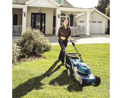 Frau bedient Rasenmäher auf Rasen vor Wohnhaus.