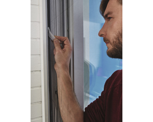 Mann montiert ein Insektenschutzgitter am Fenster