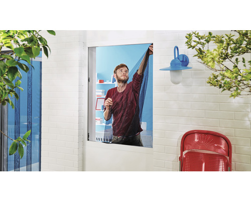 Mann befestigt ein Fliegengitter an einem Fenster, um Insekten fernzuhalten