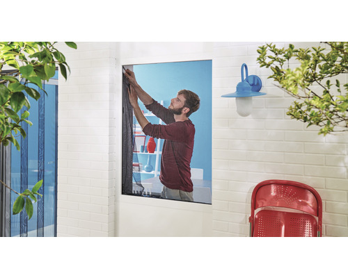 Mann montiert Insektenschutzgitter am Fenster eines Hauses mit Ziegelwand und Aussenbeleuchtung