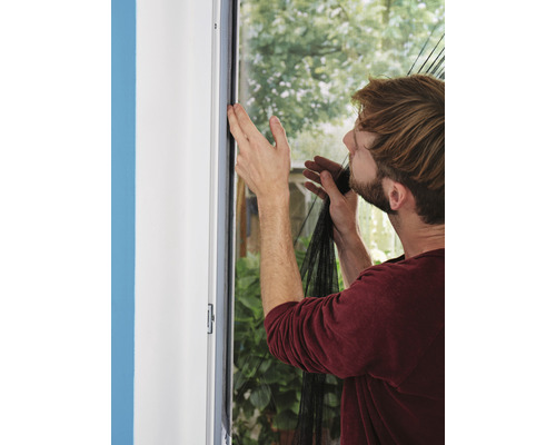 Un homme fixe une moustiquaire sur un cadre de fenêtre.