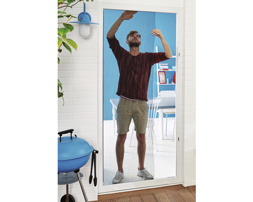 Un homme installe une moustiquaire sur une porte de terrasse.