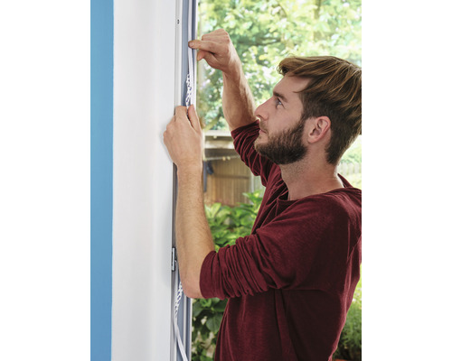 Un homme fixe une bande d''étanchéité sur le cadre de la fenêtre pour l''étanchéité.