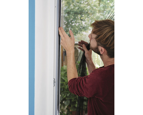 Mann befestigt ein Insektenschutzgitter an einem Fensterrahmen.