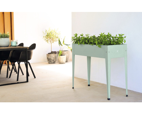 Scène avec un potager surélevé en métal, planté de plantes vertes, ainsi que des plantes en pot et une table avec des chaises