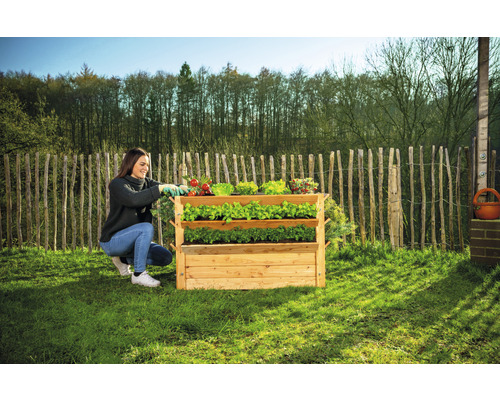 Femme travaille dans le jardin avec un potager surélevé à trois niveaux en bois pour herbes et légumes