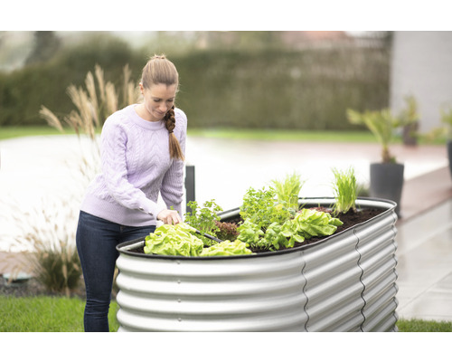 Femme travaille dans le jardin avec un potager surélevé en métal et différents légumes.