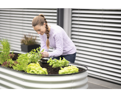 Une femme jardine dans un potager surélevé avec des légumes et des herbes aromatiques sur une terrasse.