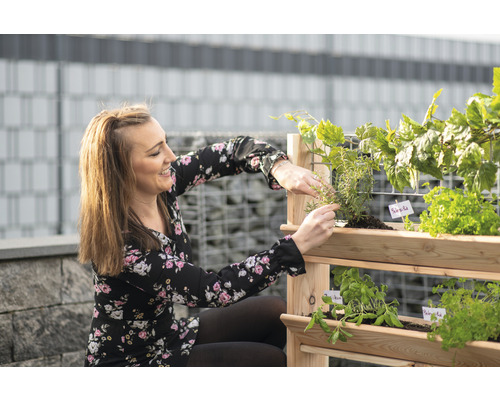 Femme entretenant des herbes aromatiques dans un support à herbes en bois pour le jardin