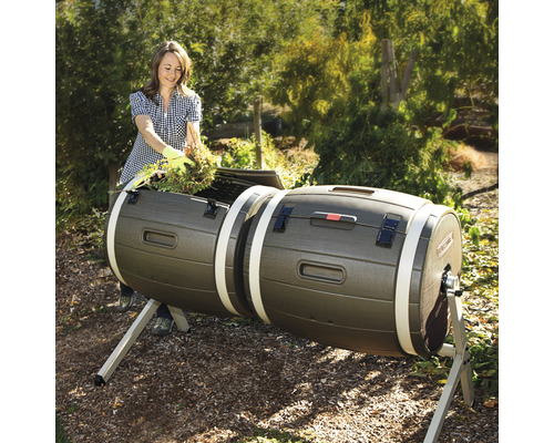 Une femme remplit un composteur rotatif double dans le jardin avec des déchets de jardin.