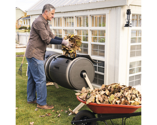 Un homme remplit un composteur de feuilles, avec une brouette à côté.