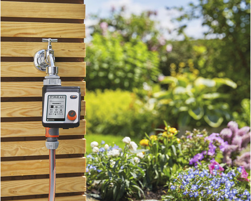 Contrôleur d''irrigation avec raccord de robinet et tuyau d''arrosage devant un jardin