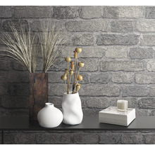 Dekorative Szene mit Vasen, Pflanzen, Kerze und Bücherstapel vor einer Steinwand.