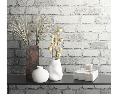 Arrangement décoratif de nature morte avec des vases, des plantes et des livres devant un mur de briques.