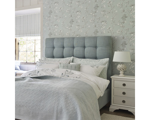 Chambre avec lit, table de chevet et papier peint floral pour une ambiance lumineuse et conviviale
