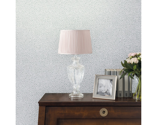 Papier peint décoratif à motif de feuilles, combiné à une lampe, un cadre photo, des livres et un bouquet de fleurs sur une table