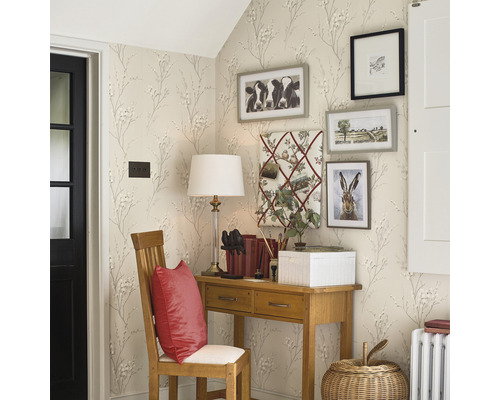 Vue en coin d''une pièce avec un bureau, une chaise et des images décoratives au mur, tapissée d''un motif de petites fleurs et de branches.